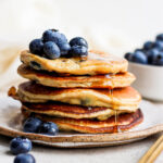 Stack of banana pancakes topped with blueberries and syrup.