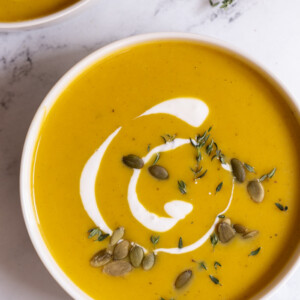 bowls filled with creamy butternut squash soup and topped with cream and pepitas