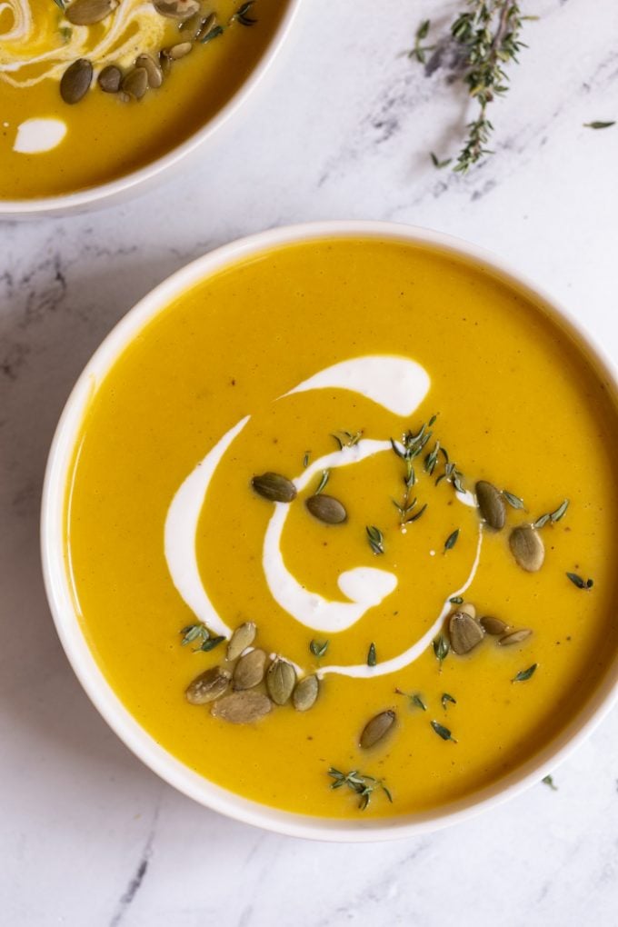 bowls filled with creamy butternut squash soup and topped with cream and pepitas
