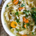 chicken noodle soup in a white bowl with crackers around it