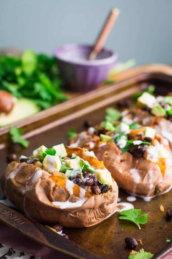 sweet potatoes stuffed with black beans and avocado on a baking tray