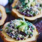 acorn squash cut in half and stuffed with quinoa nad black beans. topped with avocado and herbs