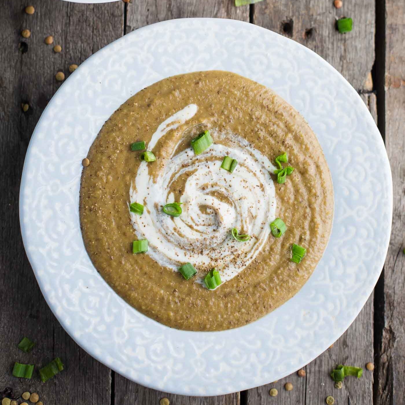 creamy lentil soup in a bowl with swirled sour cream and green onions on top