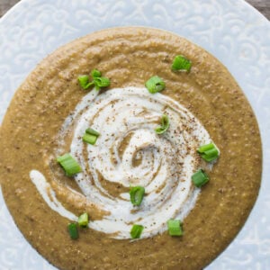 creamy lentil soup in a light blue bowl topped with sour cream and green onions