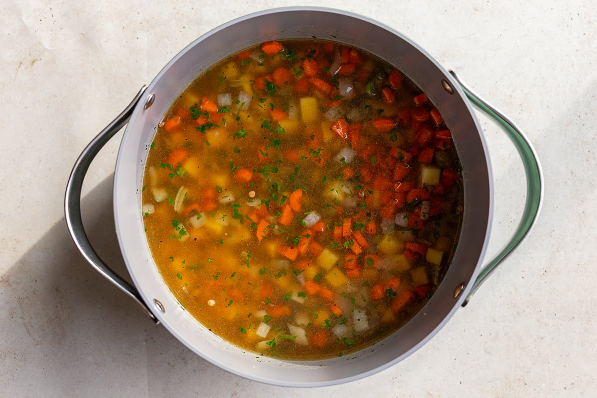 how to make lentil soup: lentils, potatoes and onions floating in broth to bring to a simmer