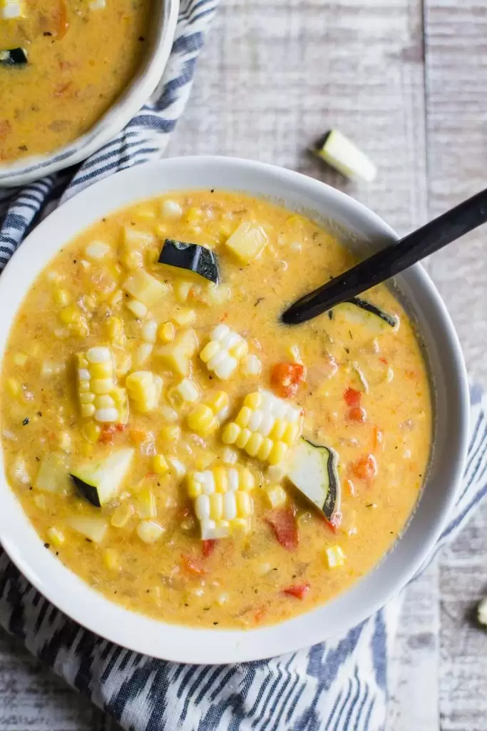 top down shot of 2 bowls of corn chowder that are both topped with fresh corn and zucchini