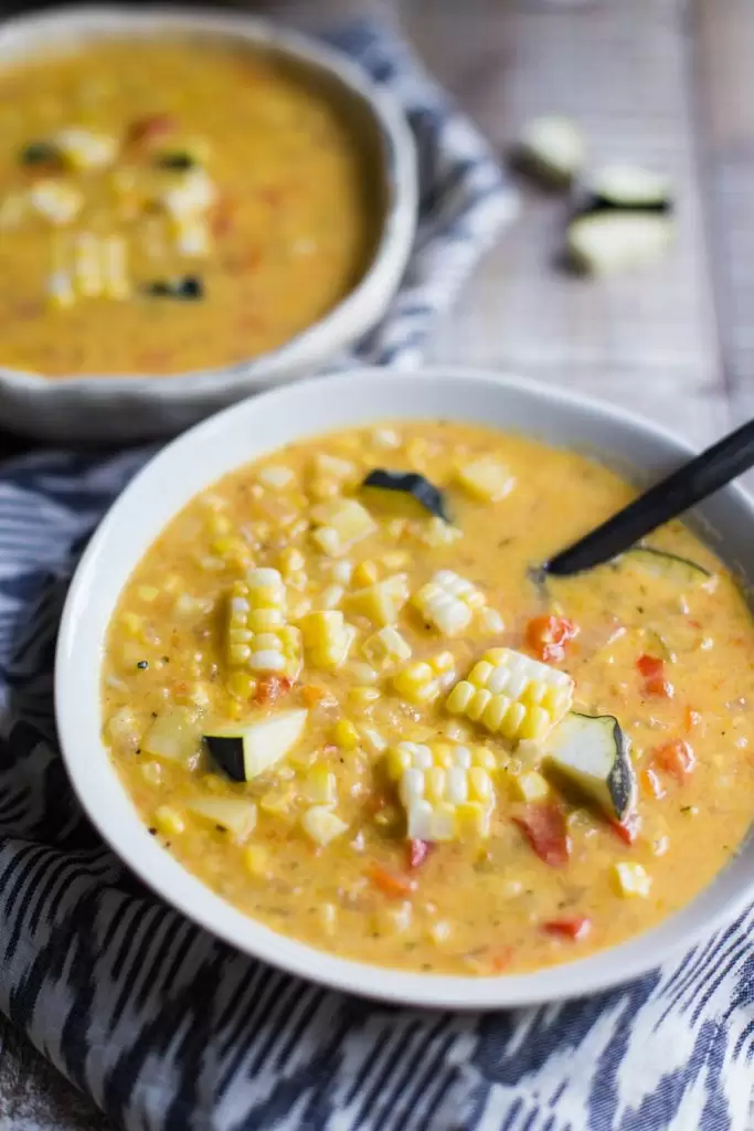 side shot of a bowl of corn chowder that's got fresh corn and zucchini on top