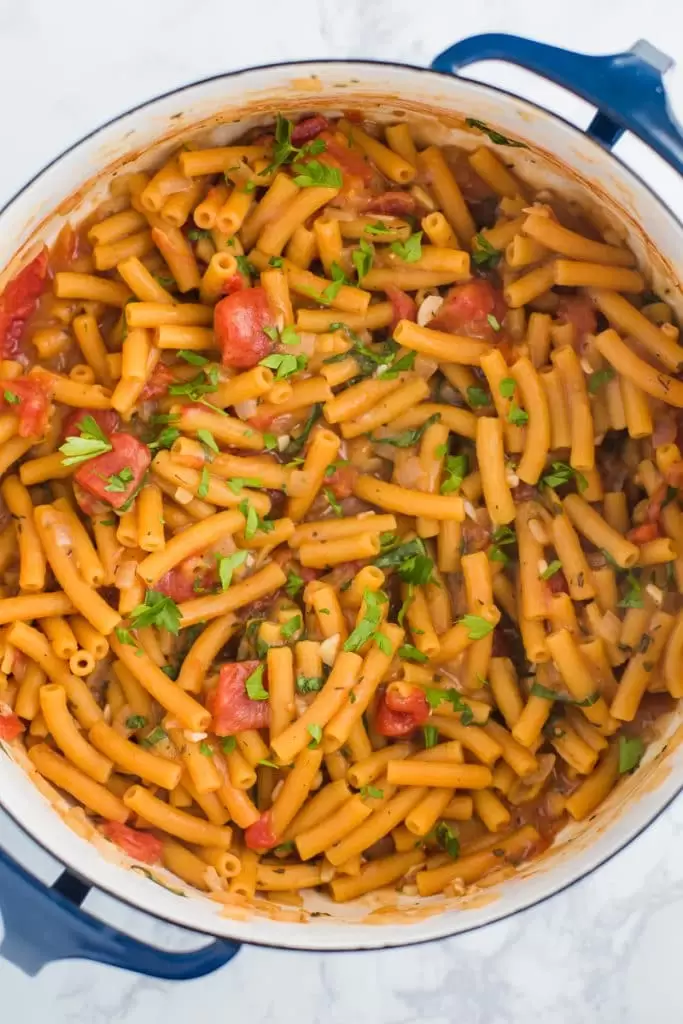 a large pot full of red lentil pasta cooked together with diced tomatoes and topped with fresh basil