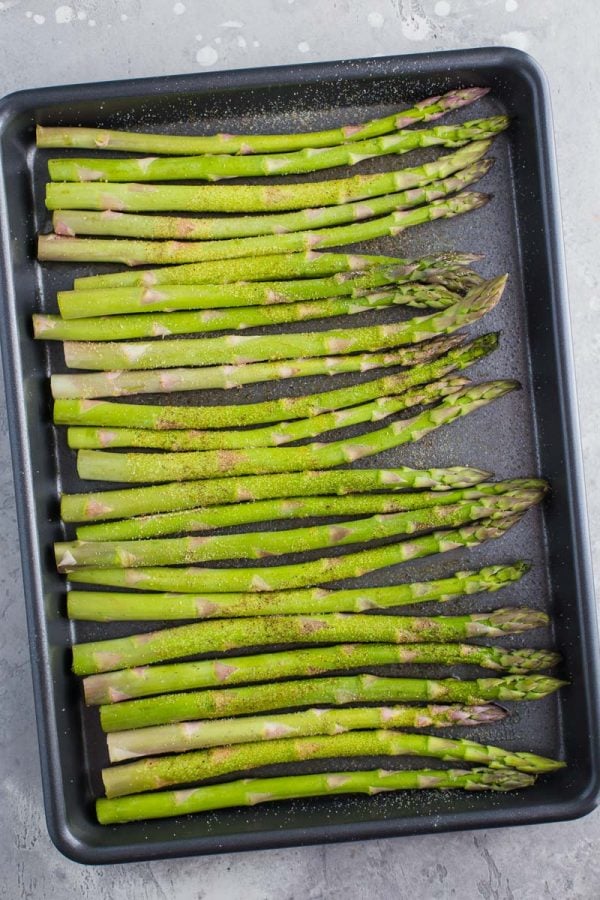 top down shot of raw asparagus spears on a dark baking sheet