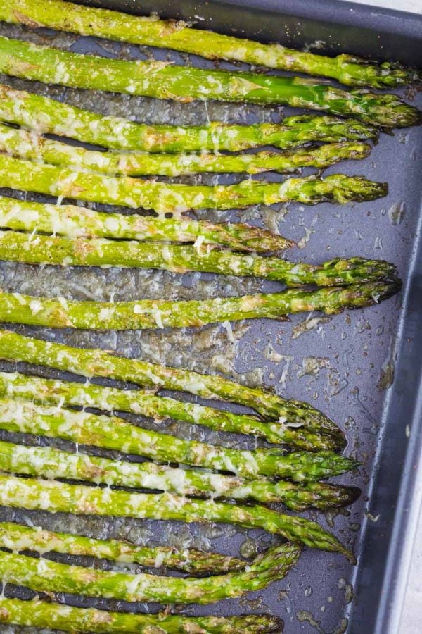 Up close shot of baked asparagus on a baking sheet with melted parmesan cheese on top