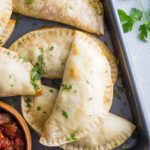 empanadas stacked up on a back tray with salsa in the corner