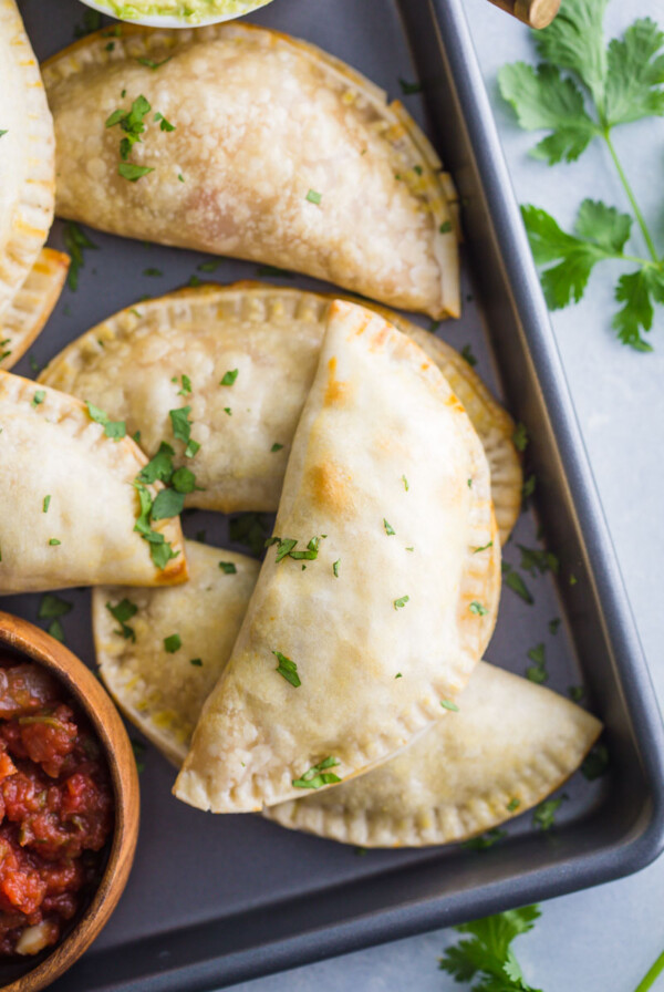 empanadas stacked up on a back tray with salsa in the corner