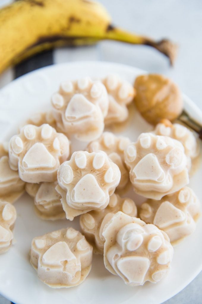 white plate with dog ice cream shaped like paw prints. peanut butter and banana in the background