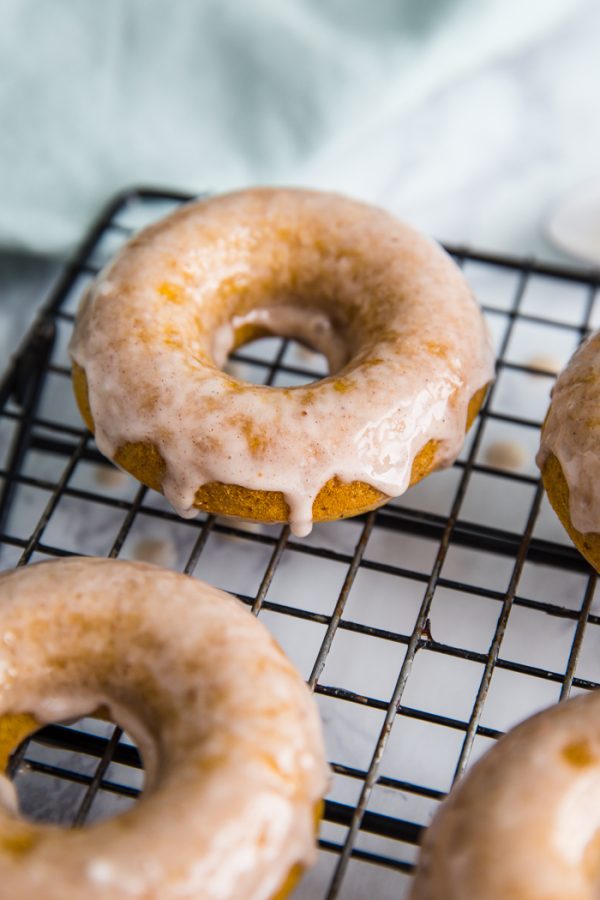 pumpkin vegan donuts with icing laying on a wire rack