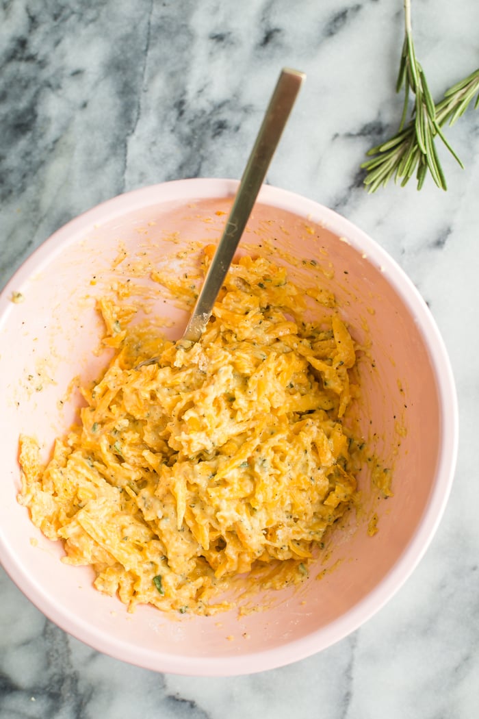 Ingredients for pumpkin fritters laid out: grated pumpkin, parmesan cheese, eggs, herbs, and spices, emphasizing ease of preparation.