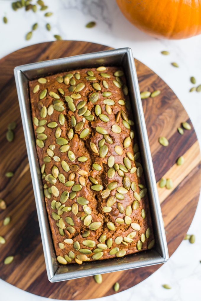 top down shot of vegan pumpkin bread in a loaf pan. the bread is covered with baked on pepitas.