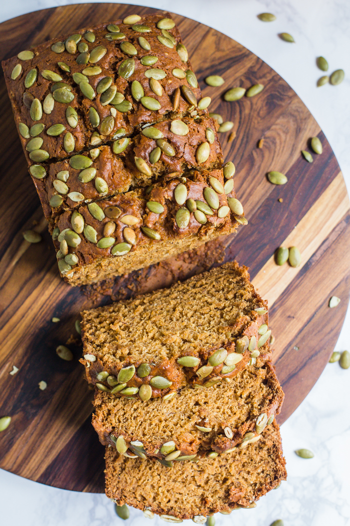 vegan pumpkin bread cut open with pepitas baked on top and a pumpkin in the background