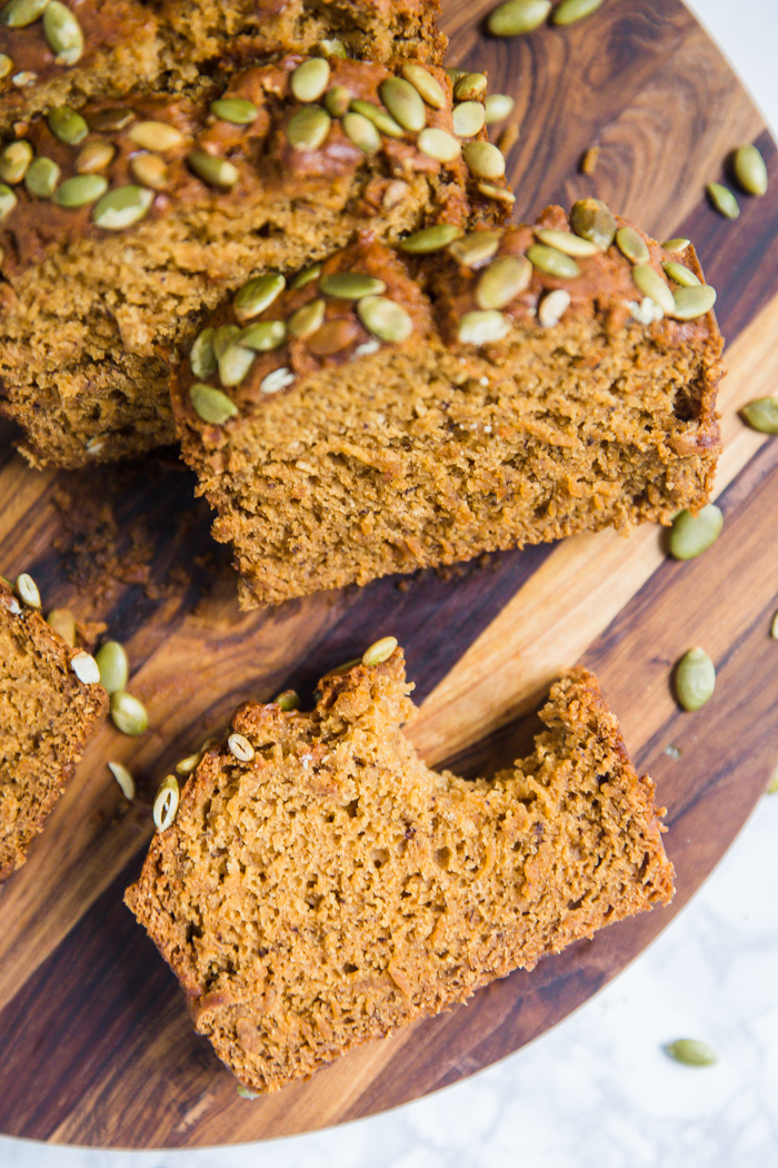 vegan pumpkin bread cut open with pepitas baked on top and a pumpkin in the background