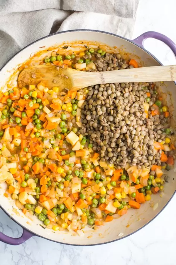 cooked lentils and sauteed veggies inside of a purple skillet with a wood spoon on the side