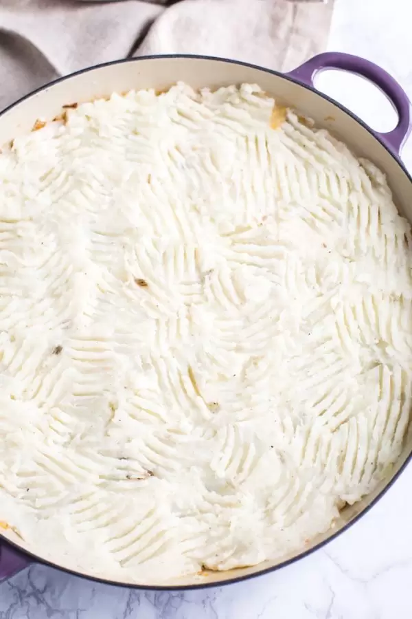 vegetarian pot pie with fresh mashed potatoes on top and fork indentions all in the top. Inside of a purple skillet and sitting on a marble baord