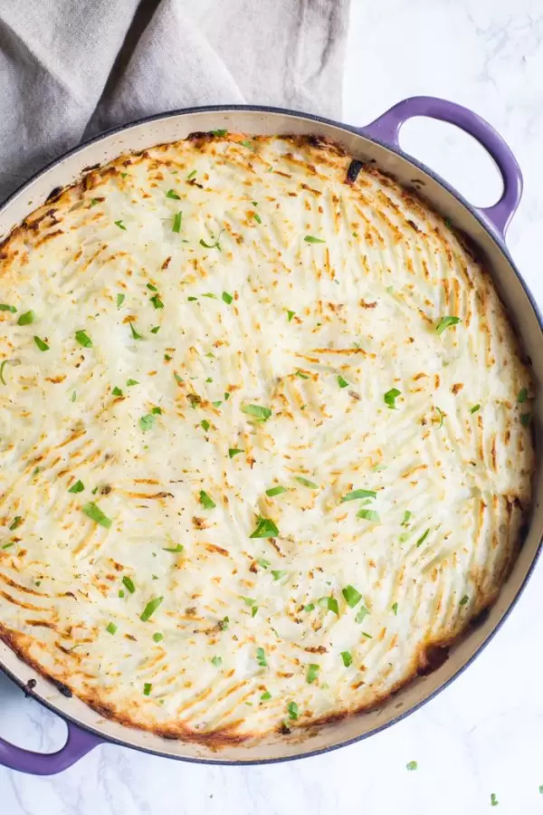 vegetarian pot pie with fresh mashed potatoes on top and fork indentions all in the top. Inside of a purple skillet and sitting on a marble baord
