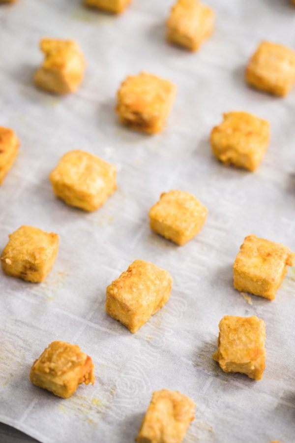 crispy cubes of tofu lined up on a baking sheet that's lined with parchment paper