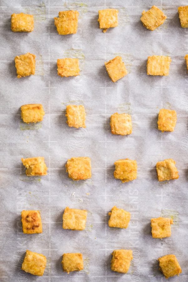 top down shot of crispy cubes of tofu lined up on a baking sheet that's lined with parchment paper