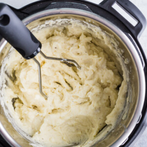 mashed potatoes in an instant pot with a potato masher on the side