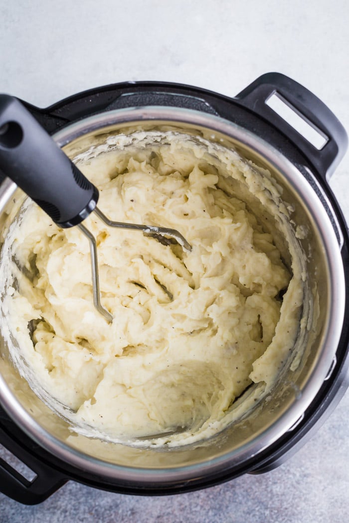 mashed potatoes in an instant pot with a potato masher on the side