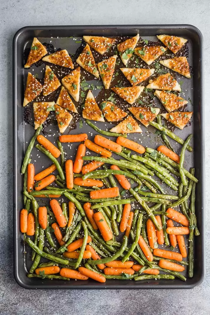 large sheet pan with triangles of marinated tofu on the top and carrot sticks + green beans on the bottom