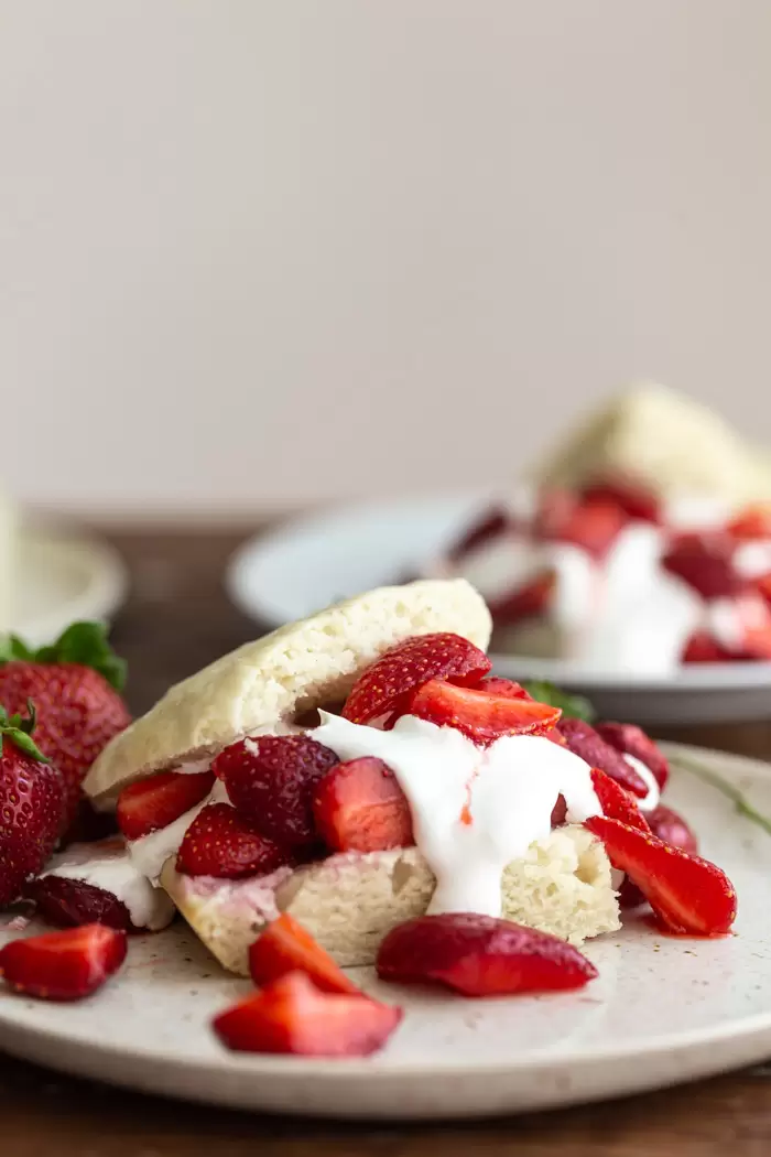side shot of shortcake cut in half and topped with whipped cream and sliced strawberries sitting on a wooden table