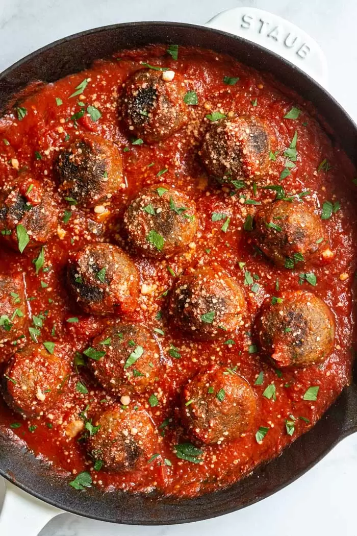 white skillet filled with vegan meatballs and sprinkled with vegan parmesan and fresh parsley