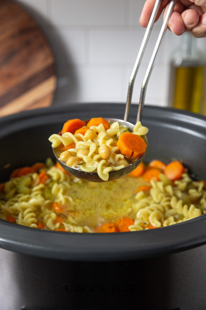 chickpea noodle soup being scooped out of a crockpot