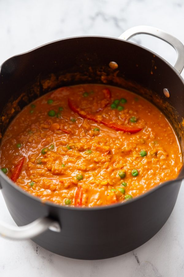red lentil curry with red bell pepper and green peas in a large pot