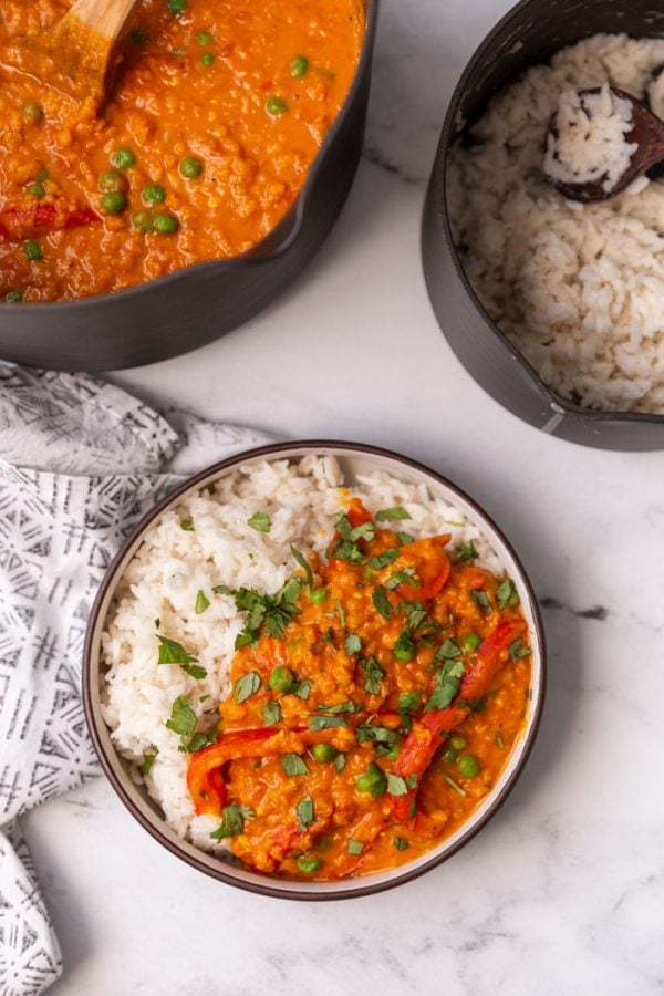 lentil curry served over white rice in a bowl with a large pot of curry and coconut rice in  small pot