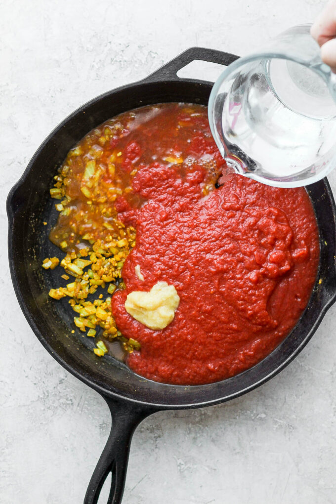 Adding water to lentils and crushed tomatoes.