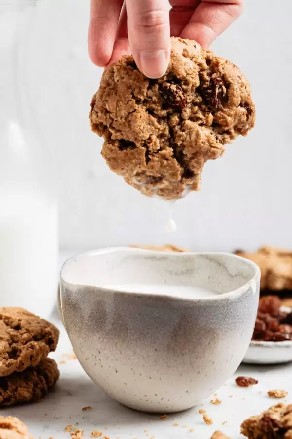 vegan oatmeal raisin cookies being dipped in a mug of milk