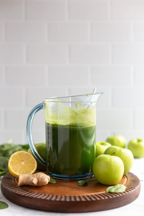 pitcher full of freshly squeezed green juice on a wood board with a white background