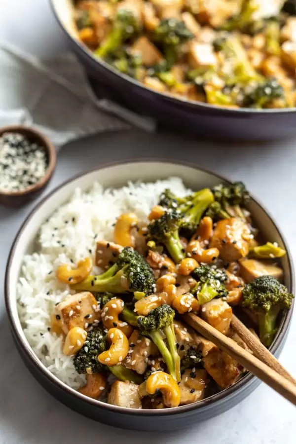 cashew stir fry over white rice in a bowl with chopsticks sticking out