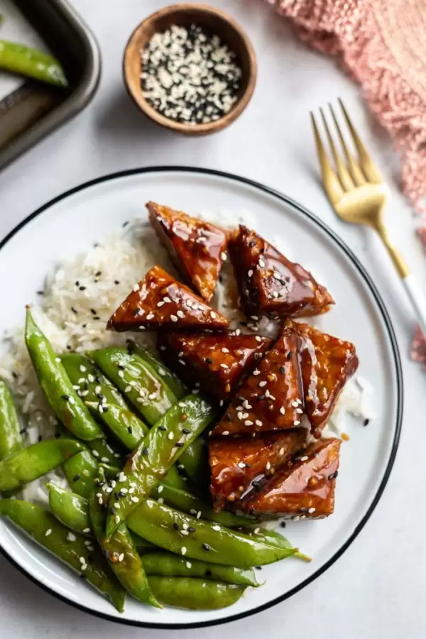 smoked tempeh and sugar snap peas on white rice in a white bowl
