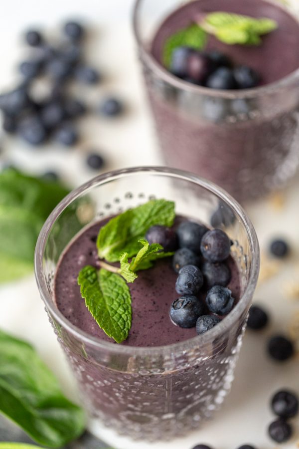 up close shot of a blueberry smoothie with mint and fresh blueberries on top