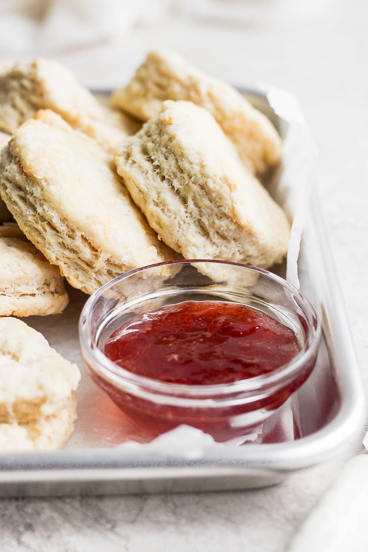 tray with biscuits stacked on it and a small bowl of grape jelly