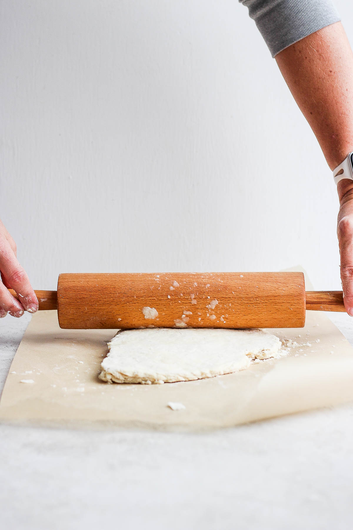 dough being rolled out with a wood rolling pin on top of parchment paper