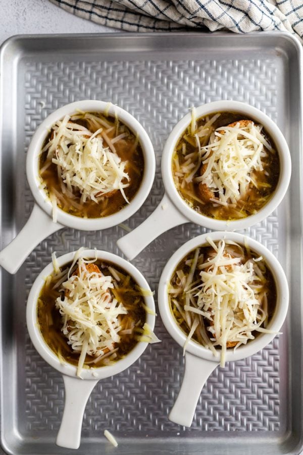 varios tazones blancos de sopa de cebolla francesa con pan y queso encima antes de que el queso se haya derretido