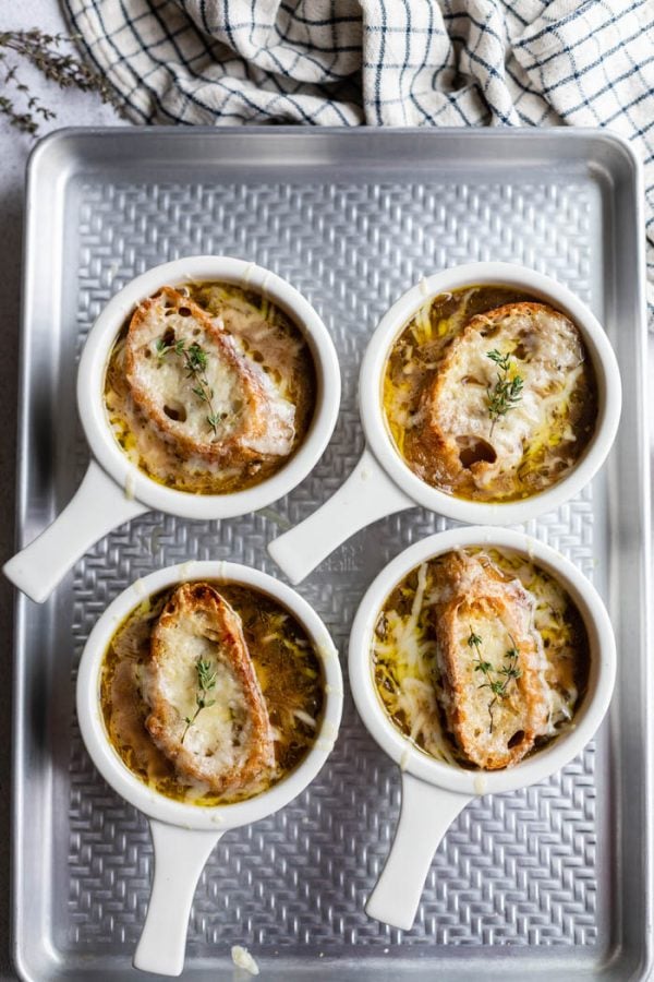 bowls of french onion soup sitting on a baking sheet with bread and der derted cheese on top