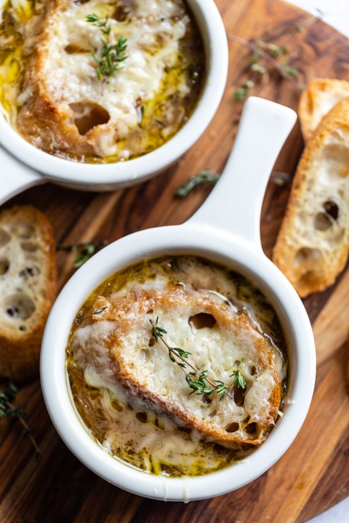 several bowls of french onion soup topped with bread, cheese, and fresh herbs