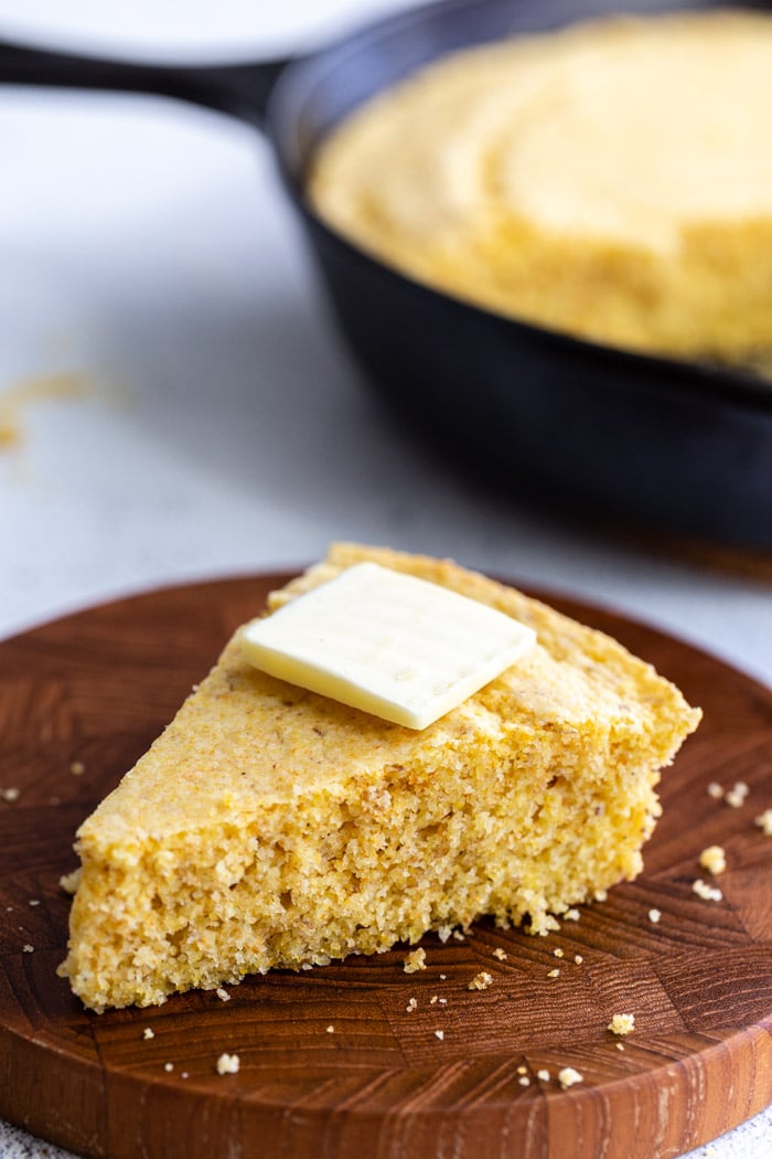 slice of cornbread on a wood board with a slice of butter on top
