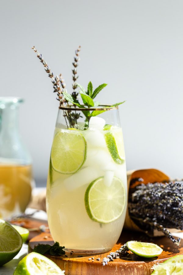 tall glass with a mojito in it garnished with lime wheels, mint sprig and dried lavender