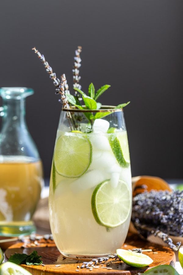 tall glass with a mojito in it garnished with lime wheels, mint sprig and dried lavender