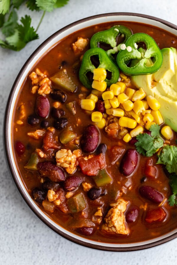 large bowl filled with tempeh chili topped with fresh corn, jalapeno and avocado